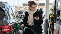 Automobiliste faisant le plein dans une station-service en France et consultant son téléphone, illustration de l’aide carburant 2026 de 100 euros.
