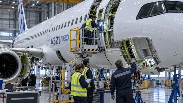 Des techniciens inspectent la partie avant d’un Airbus A321neo dans un hangar industriel, avec plusieurs panneaux du fuselage ouverts et la structure interne visible, illustrant le défaut de qualité lié au revêtement anticorrosion détecté sur plusieurs centaines d’appareils.