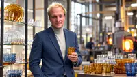 Cédric Meston, entrepreneur français et repreneur de Duralex après Tupperware France, représenté dans un environnement industriel de verrerie avec un verre ambré à la main, en référence à la stratégie de relance et de modernisation de la célèbre marque française Duralex.