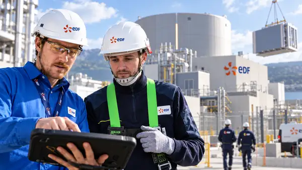 Ingénieurs EDF en tenue de sécurité sur un site nucléaire moderne avec infrastructure de petit réacteur modulaire, logo EDF visible sur les équipements et les bâtiments, illustrant le projet du groupe de construire 10 SMR en Europe d’ici 2035 avec la technologie NUWARD.