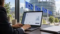 Entrepreneur devant un ordinateur affichant un formulaire et une carte de l’Europe, avec des drapeaux de l’Union européenne et un bâtiment institutionnel en arrière-plan, pour illustrer le projet EU Inc. de création d’entreprise européenne.