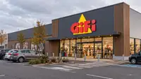 Illustration générée par IA représentant la façade d’un magasin GiFi dans une zone commerciale, avec son enseigne rouge et jaune, une entrée vitrée et un intérieur éclairé laissant apparaître des rayons de décoration. Plusieurs voitures sont stationnées devant le bâtiment, sous un ciel couvert, dans une ambiance automnale.