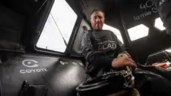 Benjamin Dutreux dans le cockpit d’un IMOCA aux couleurs de 4CAD Group, les mains posées sur un cordage près d’un winch. La photographie montre les équipements de manœuvre, les parois en carbone et les ouvertures du cockpit, au cœur de l’environnement de travail à bord d’un voilier de course au large.