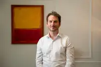 Christophe Bouron, cofondateur d’Ofelia Agentic, photographié debout dans un intérieur professionnel, vêtu d’une chemise blanche, devant une œuvre abstraite rouge et jaune.