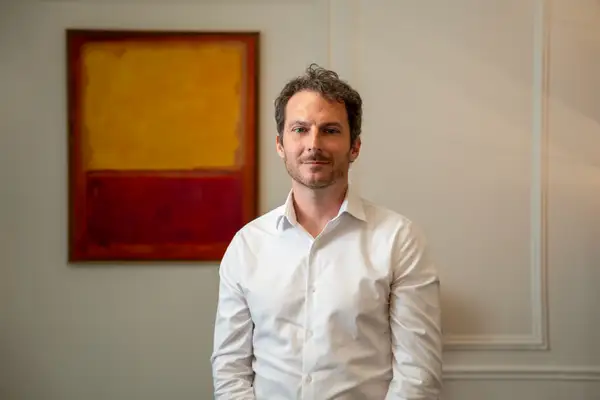 Christophe Bouron, cofondateur d’Ofelia Agentic, photographié debout dans un intérieur professionnel, vêtu d’une chemise blanche, devant une œuvre abstraite rouge et jaune.