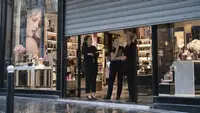 Trois salariées réunies à l’entrée d’une parfumerie française au rideau métallique partiellement baissé, entourées de vitrines de cosmétiques, une scène illustrant les inquiétudes liées au projet de rachat de Marionnaud et à l’avenir de ses magasins.