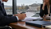 Deux professionnels examinent des documents financiers sur une table avec une calculatrice et un dossier bleu, devant une fenêtre donnant sur le palais Bourbon et un drapeau français à Paris.