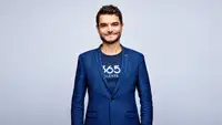 Portrait de Loïc Michel, cofondateur et directeur général de 365Talents, portant une veste bleue et un tee-shirt au logo de l’entreprise, sur fond gris clair.