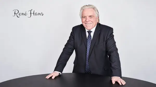 Portrait de René Hans en costume sombre, debout derrière une table noire sur fond gris clair, dans un visuel éditorial consacré à son parcours, à Capital Initiative et à son engagement en faveur du financement des TPE et PME françaises.