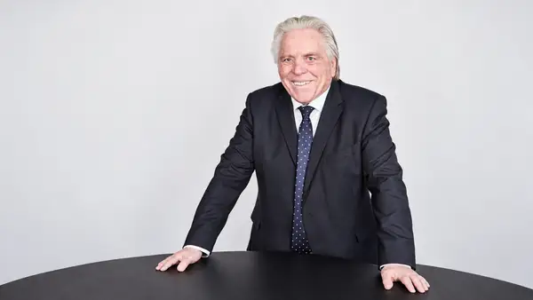Portrait de René Hans, expert-comptable, entrepreneur et fondateur de Capital Initiative, en costume sombre derrière une table noire sur fond gris clair, dans le cadre d’un article consacré à son parcours, à ses convictions et à son engagement en faveur du financement des TPE et PME françaises.