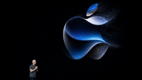 Logo Apple lumineux projeté sur une scène sombre lors d’une présentation technologique, avec un dirigeant en bas de l’image.