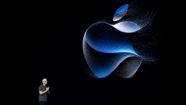 Logo Apple lumineux projeté sur une scène sombre lors d’une présentation technologique, avec un dirigeant en bas de l’image.