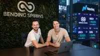 Les deux dirigeants de Bending Spoons posent dans les bureaux de l’entreprise, devant son logo et des écrans évoquant une introduction au Nasdaq.