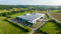 Illustration d'une usine moderne avec des panneaux solaires et des éoliennes, symbolisant la décarbonation industrielle et la transition vers le zéro fossile.