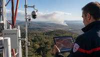 Système FireTracking installé sur un point haut avec caméras de surveillance, opérateur consultant une carte sur tablette et départ de fumée détecté au loin.