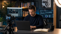 Infopreneur travaillant sur un ordinateur dans un studio de création équipé d’une caméra, d’un microphone et d’écrans affichant une formation en ligne et des données de performance.