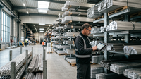 Illustration d'une main tenant des échantillons de matières premières PME (métaux, plastiques) avec un graphique boursier en arrière-plan, symbolisant la volatilité des prix et la gestion des risques pour les PME.