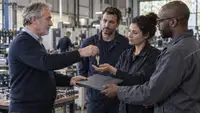 Un dirigeant de PME remet les clés et le dossier de son entreprise à trois salariés dans un atelier industriel, illustrant la transmission d’entreprise encouragée par le futur Pacte Papin.