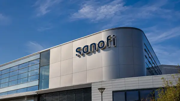 Façade moderne d’un bâtiment Sanofi avec le logo du groupe pharmaceutique sous un ciel bleu.